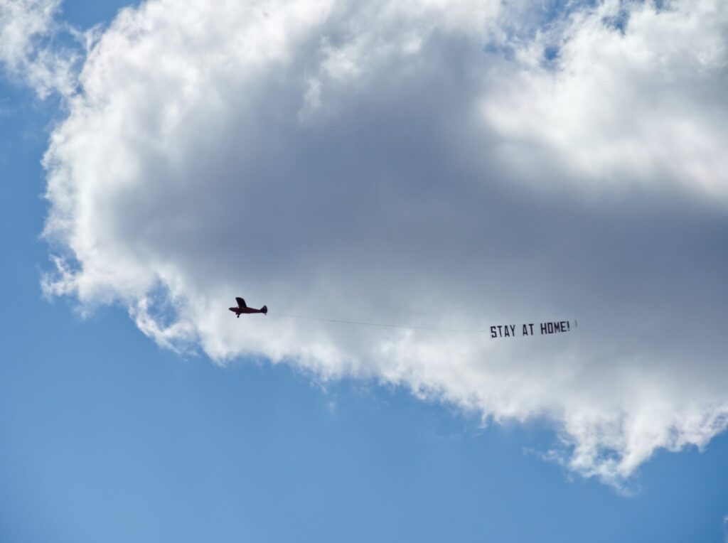 Stay at Home - Flugzeug mit Corona Banner am blauen Himmel über der Bauernhof Kita