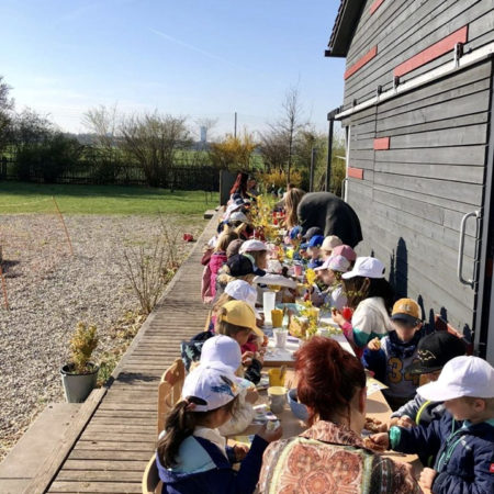 Bauernhof-Kita-Ostern-2022: Kinder sitzen auf der langen Bank in unserem Garten - Oster-Fest-Frühstück